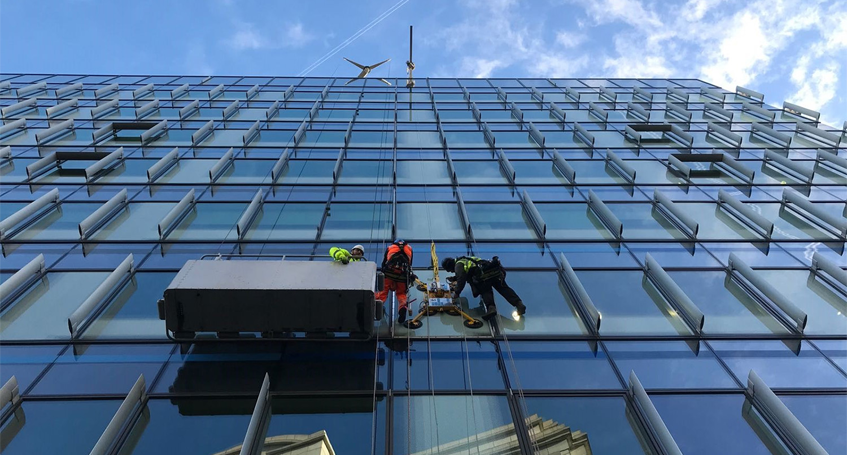 Workers on Platform Performing Commercial Glass Repair on a Modern Building Facade
