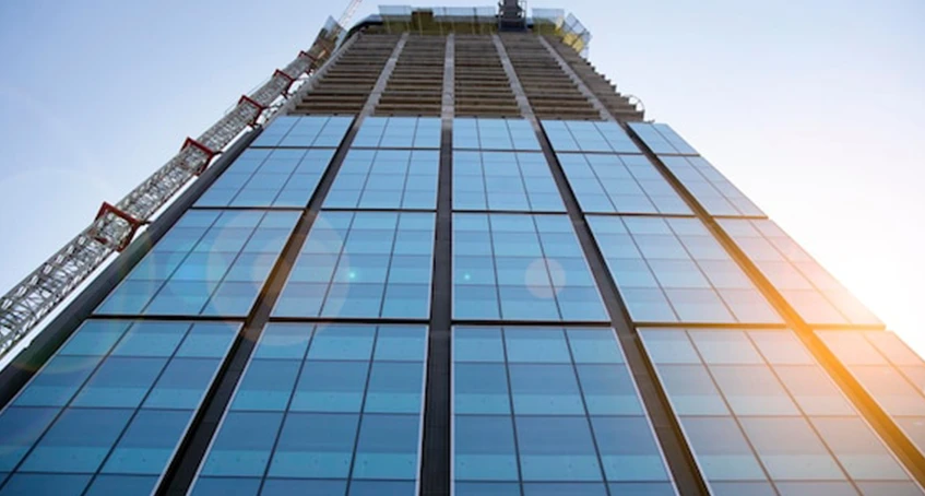 Skyscraper with Glass Panels and Construction Crane in Bright Sunlight